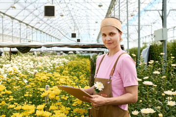 Waist up portrait of young woman holding clipboard while enjoying work in flower plantation copy space