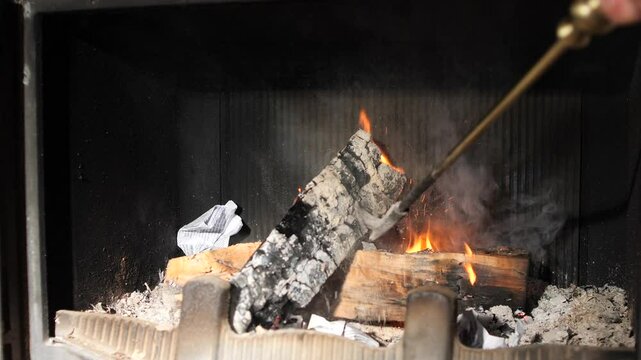 person skillfully adjusting a burning log in a cozy fireplace setting