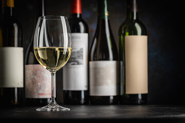 A dark, elegant still life of white wine in a glass with wine bottles and fresh grapes in the background. Perfect for wine-themed compositions