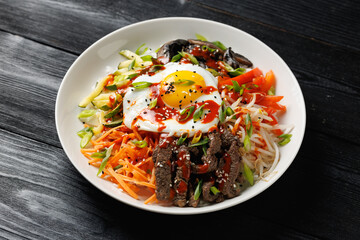 Traditional Korean dish Bibimbap with rice, vegetables beef and egg in a white plate