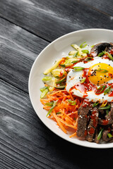 Traditional Korean dish Bibimbap with rice, vegetables beef and egg in a white plate