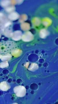 Vertical video. Flower essence. Gel fluid. Defocused blue white green neon color natural blossom glitter texture oil bubble abstract background.