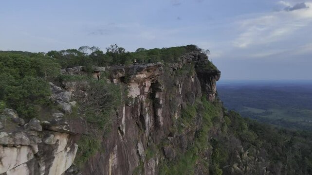 Drone flies backwards from below the Pedra de Mao de Deus rock at sunset in Tepequem, Roraima, Brazil
