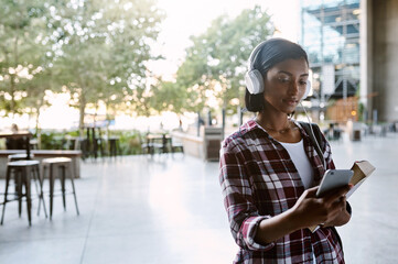 Headphones, girl and student walking with phone for listening to radio, educational podcast and book. Reading, indian person and smartphone on campus with sound app, audio playlist and study music