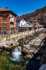 The river. Abandoned houses and other buildings, lit by sunlight, street view, Pirin village and mountain, Bulgaria