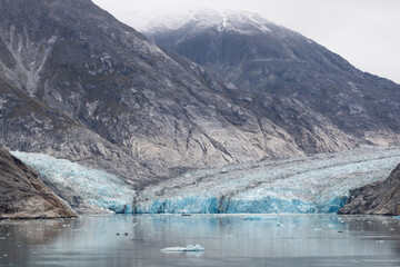 Glacier ice nested in between the mountain and water, rugged and beautiful with striations and texture.