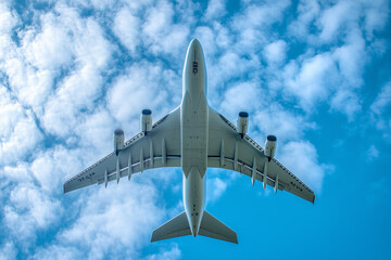 A large, white airplane flies against a cloudy blue sky.
