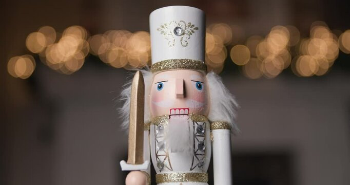 royal Nutcracker figurine dressed in a white costume, holding a sword, standing proudly and rotating against golden bokeh lights 
