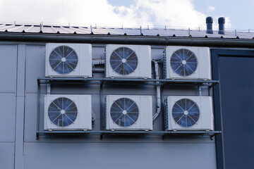 Industrial air conditioning units installed on the wall of a building, with a clear blue sky and clouds in the background. HVAC system.