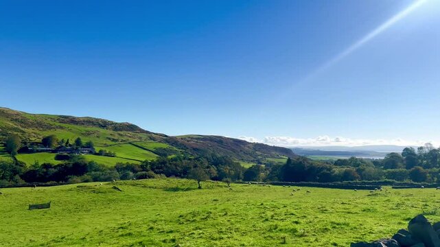 A breathtaking video of a rustic stone farmhouse, green fields set against rolling green hills under a bright blue sky. Enjoy as camera pans across this idillic scene.