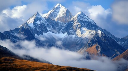 Fototapeta premium Snow-capped mountain peaks with mist drifting across the rugged landscape under a clear blue sky