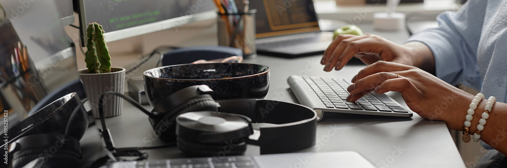 Poster website header shot of female hands typing on computer keyboard and headphones lying on working desk