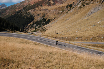 A cyclist rides along a winding road through the mountains. The road is surrounded by dry grass and hills. A cyclist is practicing cycling.Sport motivation.Adventure travel on bike.Mountain background