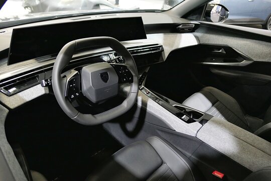 Interior detail of modern french plug in hybrid PHEV mid sized crossover SUV car Peugeot 5008 Hybrid. Dashboard with displays, driving wheel, front seats and central tunnel visible. 