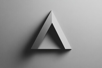 Fototapeta premium A triangular sculpture stands against a smooth gray backdrop, creating a striking shadow that enhances the minimalist aesthetic
