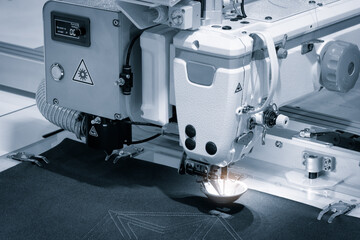 A sewing machine with a light shining on it. The machine is in a factory setting, sewing factory, clothing manufacturing