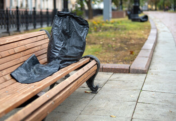 black garbage bag rests on a park bench, symbolizing neglect and environmental issues. It contrasts...