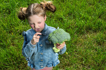 Child girl points at broccoli with disgust.