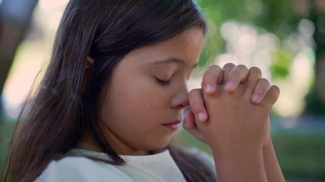 Girl with eyes closed, hands clasped in a prayer position, deeply focused and serene, symbolizing spirituality, hope, and faith. peaceful outdoor atmosphere