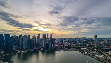 Fototapeta premium Scenic aerial view of Singapore iconic skyline at dusk. Towering skyscrapers, illuminated by setting sun. Marina Bay waterfront with its bustling activity and vibrant lights. SkyPark Observation Deck