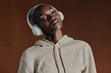 Black woman, hoodie and headphones for music in studio portrait, training and fitness by background. Person, model and style with jacket, streetwear and streaming with clothes for winter in Nigeria