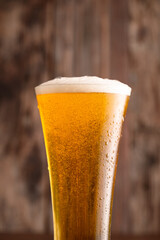 Glass of beer with foam and water drops on wooden background