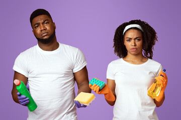 Domestic Duties Concept. Portrait Of Displeased Black Man And Woman With Cleaning Tools In Hands Over Pink Background, Free Space