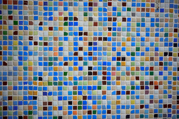 Fototapeta premium Close-up of a vibrant mosaic tile wall featuring a mix of blue, orange, brown, and white tiles arranged in a random geometric pattern. 