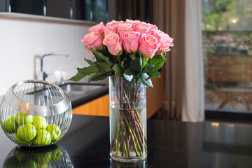 A bouquet of red roses on the kitchen table. Next to it, a metal vase with green apples. Reflection...