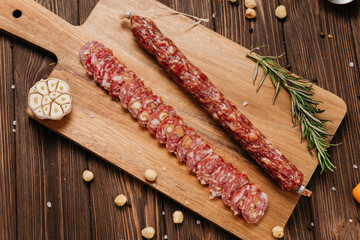 Sliced gourmet smoked salami on a wooden board with herbs, perfect for charcuterie boards and snacks
