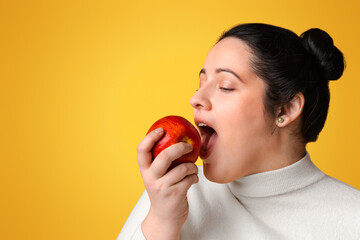 Portrait Of Young Overweight Woman Biting Red Apple, Eating Healthy Food, Dieting, Standing Over Yellow Background With Empty Space