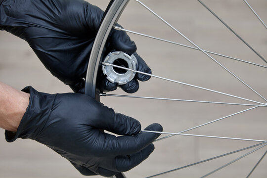 adjusting the tension of the spokes of a bicycle wheel. repairman's hands in black rubber gloves with a wrench close-up