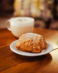 Azúcar impalpable cayendo sobre un pan dulce ubicado sobre una mesa de madera y una taza de Rooibos chai detrás