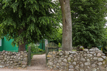 A charming, rural entrance to a stone-walled yard with an old wooden house, Poland