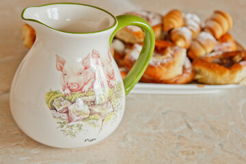 buns in a plate full of freshly baked bagels dusted with icing sugar with a ceramic jug on the kitchen table. cooking baking. croissants baking preparation stage. breakfast closeup copy space