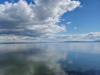 Obraz premium Serene Irish Seaside: Ocean Embankment with Clear Waters and Cloud Reflections