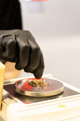 Selective focus of weighing gold jewelry with small digital scales in jewelry shop. Hand take jewelry on the digital scale, close up. Hand in black glove puts gold on scales.