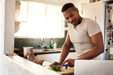 Black man, laptop and cooking in home with online recipe, cutting vegetables and meal preparation....