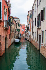 Scenic Venetian canal with traditional buildings and stone bridge. Beautiful Venice canal with colorful historic buildings, arched stone bridge, and calm water reflecting the scene.