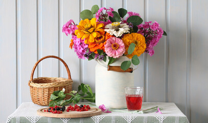 summer still life in a rural style with flowers, a drink and berries. a bouquet of zinnias and phlox. currants on a chopping board.