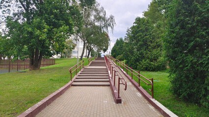 A stairway and inclined ramp with tiled floor and metal handrails was constructed to provide freedom of movement on the street for people with disabilities. Accessible environment. Nearby are trees