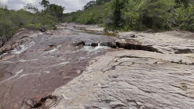 Drone flies backwards along stream leading to Cachoeira do Barata waterfall in Tepequem, Roraima, Brazil
