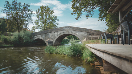 Stone bridge over a river with green grass and a wooden dock, rustic and tranquil, perfect for a summer vacation. 
