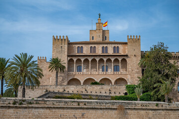 Fototapeta premium The Royal Palace of La Almudaina in Palma de mallorca with trees in front during great weather, view from the distance, Majorca