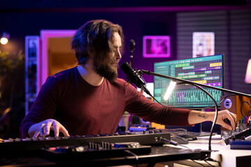 Sound engineer twisting pre amp knobs on mixing console in home studio, recording tunes and adjusting volume levels. Producer artist creating songs with midi controller piano and gear.