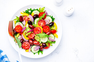 Colorful vegetable salad with olives, tomato, paprika, cucumber, onion, and herbs. White background, top view