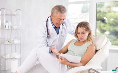 Obraz premium Mature male nurse shows clinic woman client papers for familiarization and signing of consent for injection cosmetology procedure. Medical documentation, questionnaire, patient survey