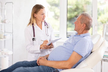 Female nurse carries out questionnaire survey of elderly male patient about allergic reactions and...
