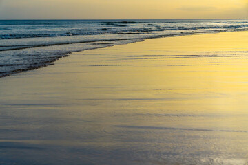 Golden light reflecting off the wet sand as gentle waves roll in.