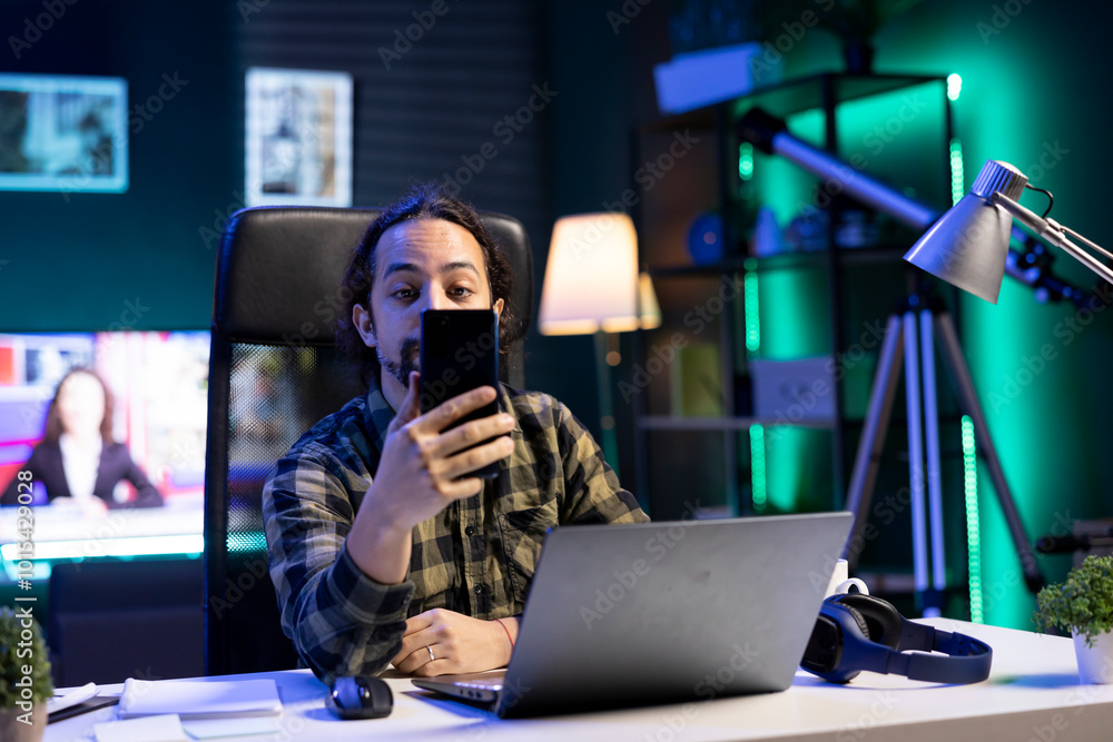 Poster portrait of a young man using his mobile device to communicate with friends while seated in front of